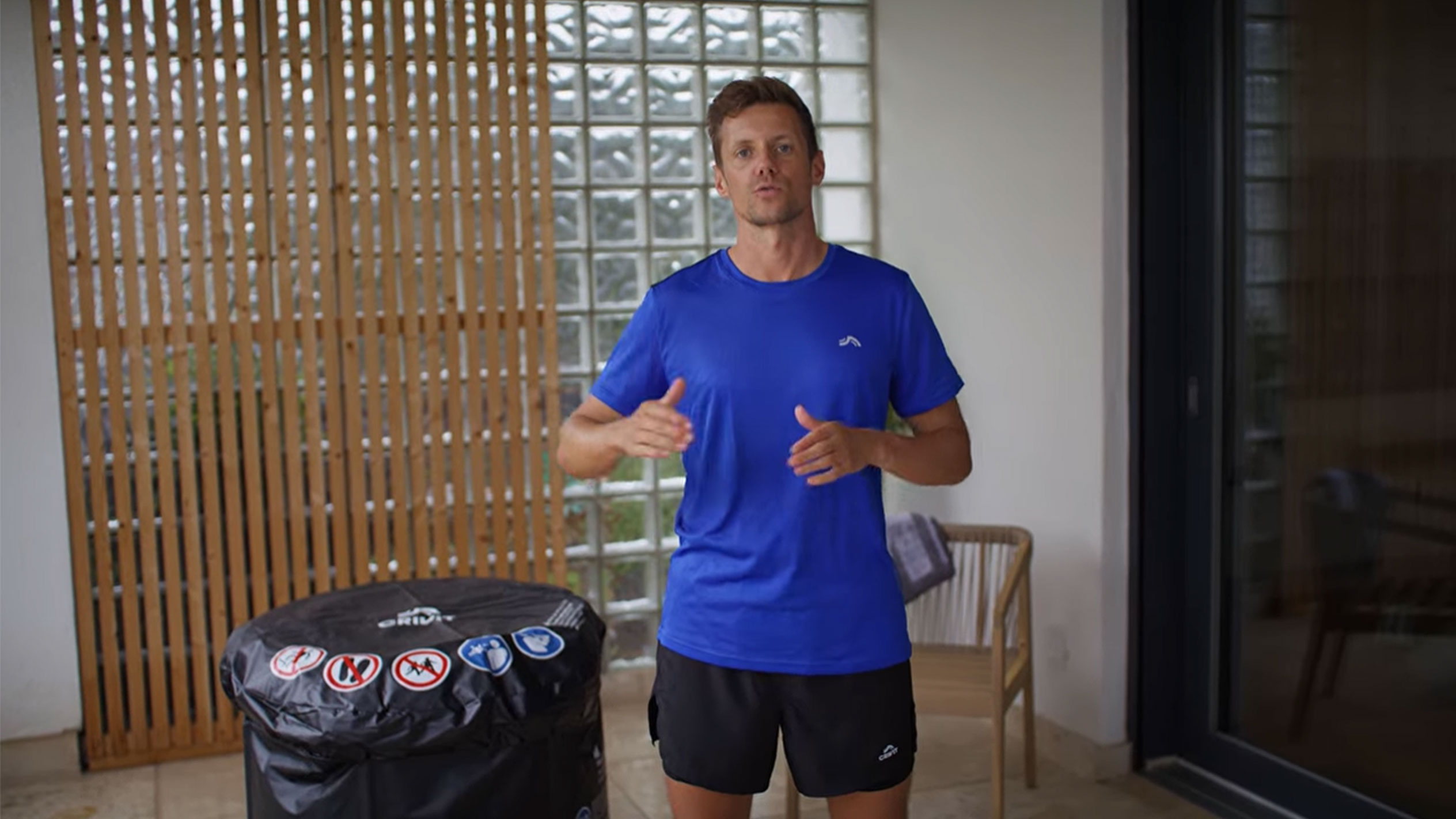 Vyras mėlynais marškinėliais ir juodais šortais, šalia juodo kubilo dangčio.