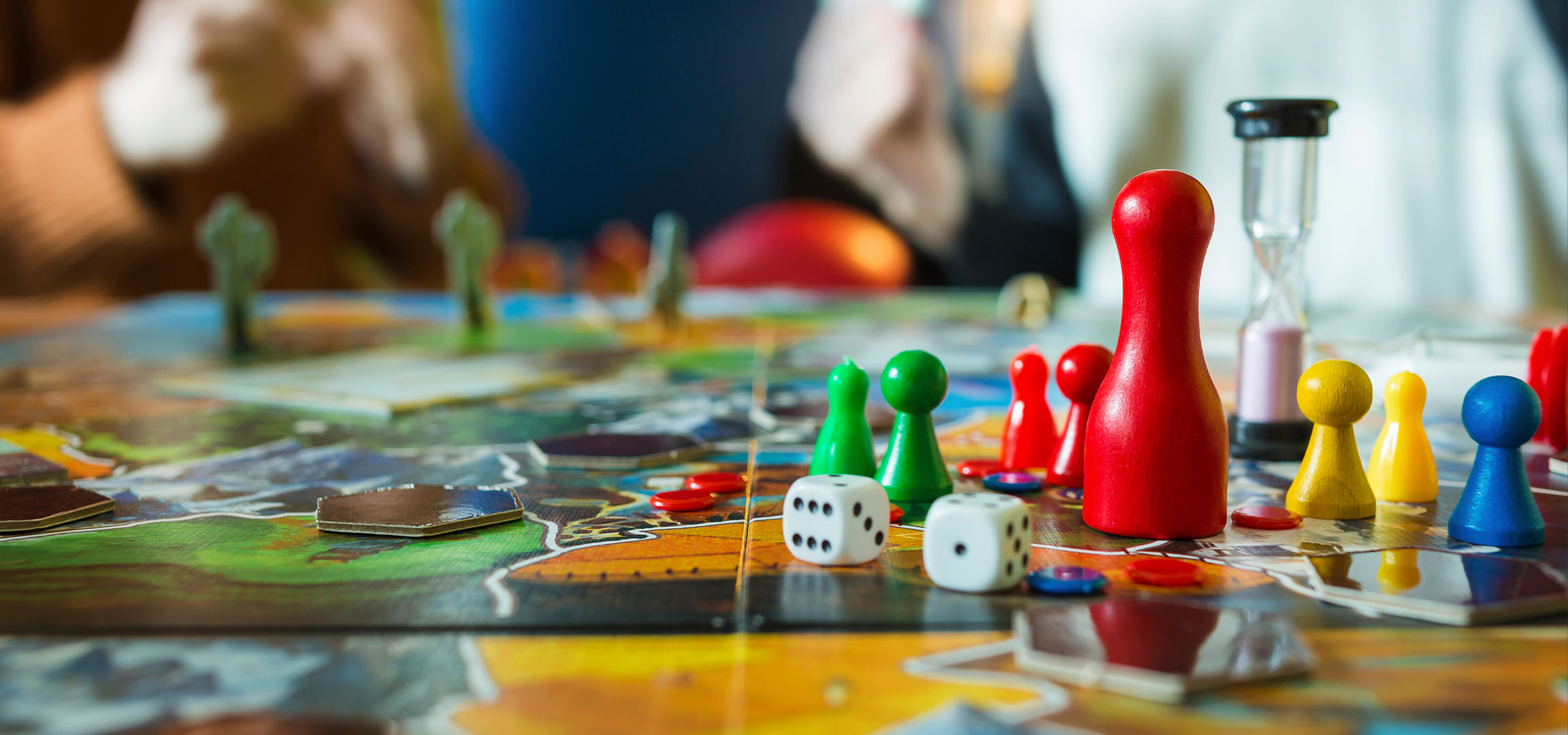 Spalvingi stalo žaidimo elementai, įskaitant raudonus, žalius, geltonus ir mėlynus pėstininkus, su kauliukais.