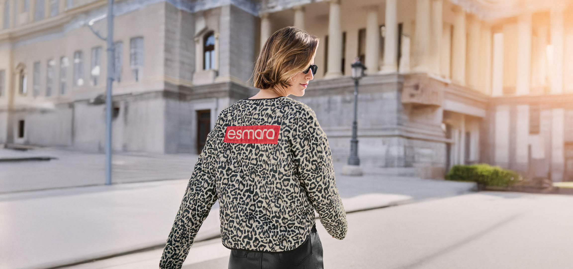 Moteris su Esmara leopardo rašto striuke, akiniais nuo saulės, miesto gatvėje.