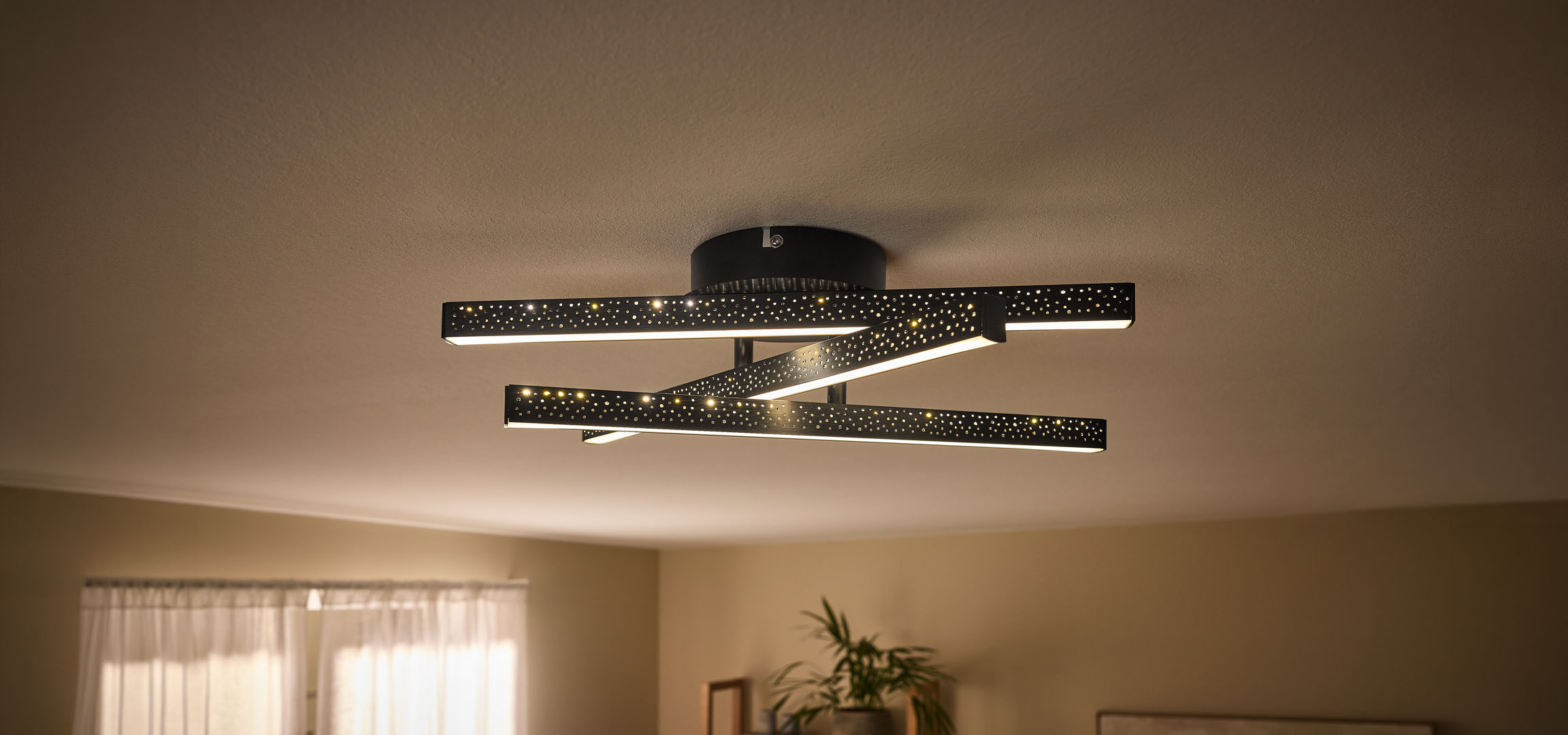 Modernus LED lubų šviestuvas su juodais, perforuotais strypais ir šilta šviesa.