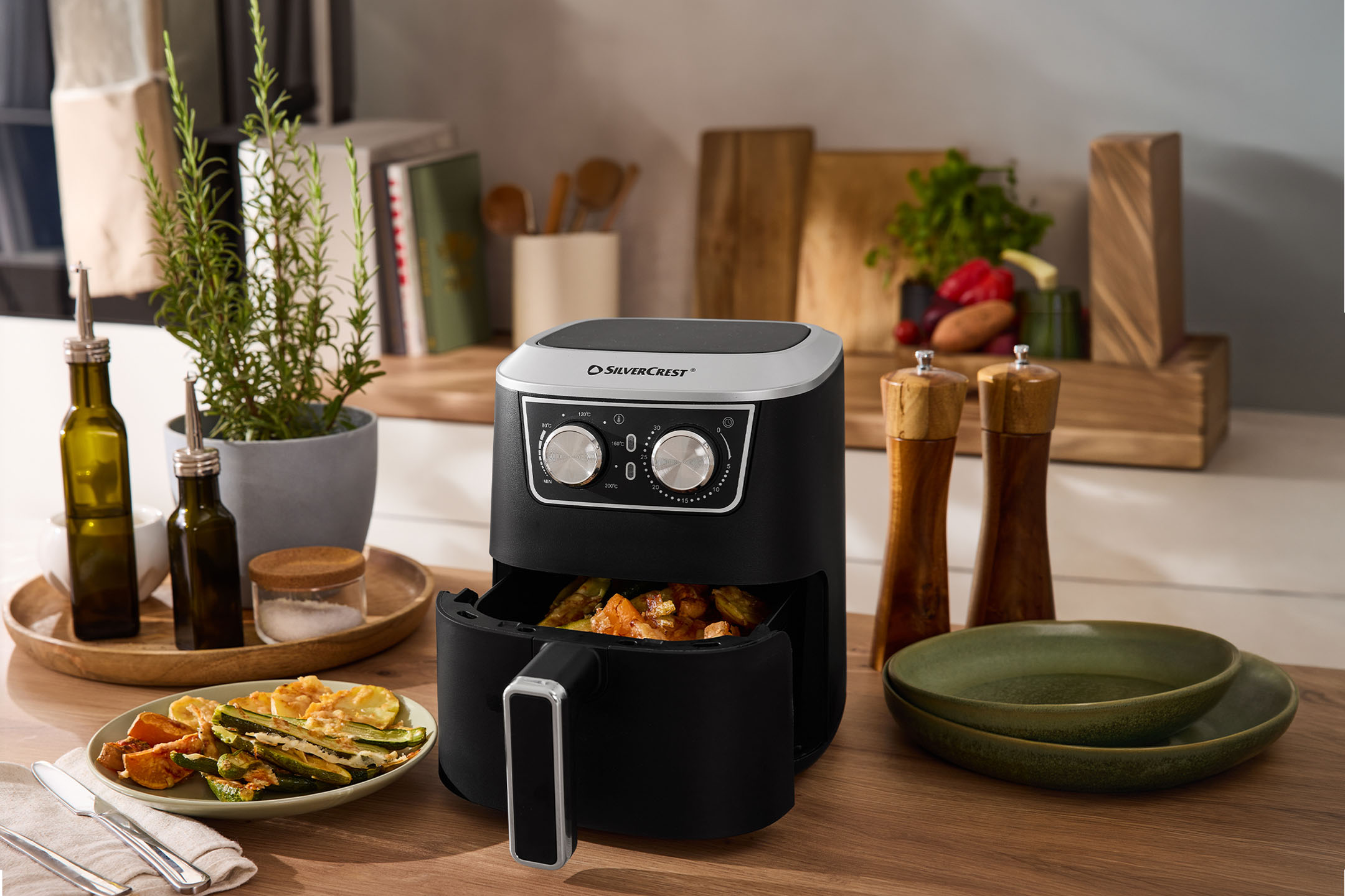 Juoda oro gruzdintuvė su daržovėmis, prieskoniais ir indais ant medinio stalviršio.