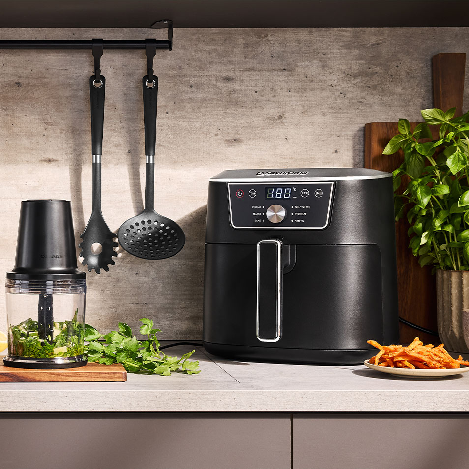 SilverCrest oro gruzdintuvė ir maisto smulkintuvas ant virtuvės stalviršio su šviežiomis žolelėmis ir saldžiųjų bulvių fri bulvytėmis.