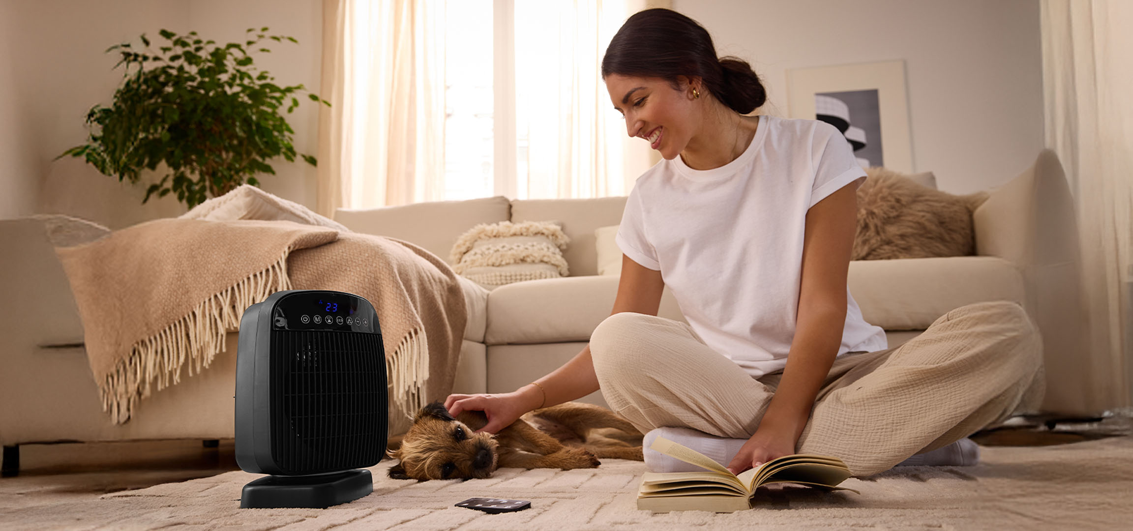 Moteris žaidžia su šunimi prie elektrinio šildytuvo svetainėje.