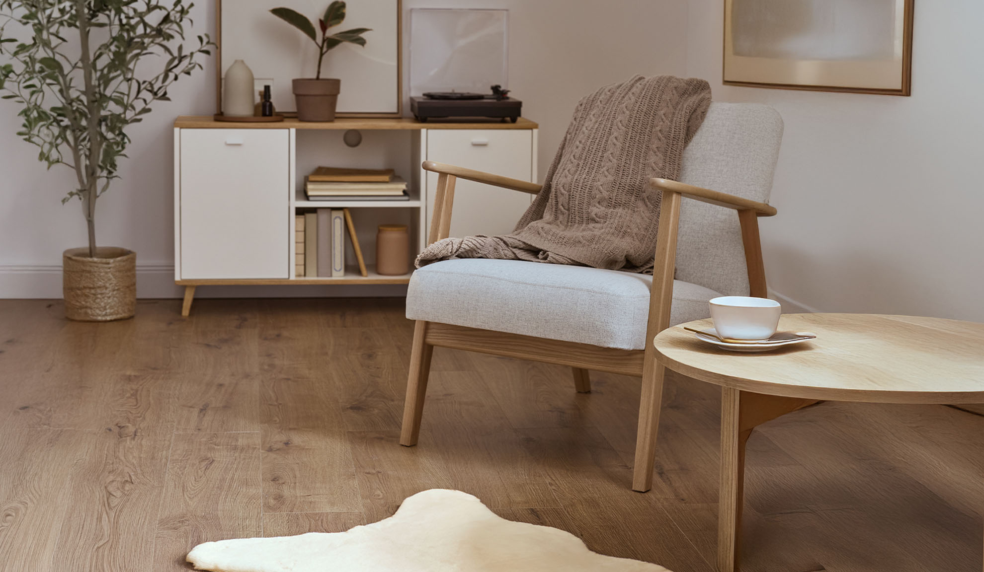 Patogus fotelis su pledu, mediniu kavos staliuku ir daiktadėže šviesioje svetainėje.