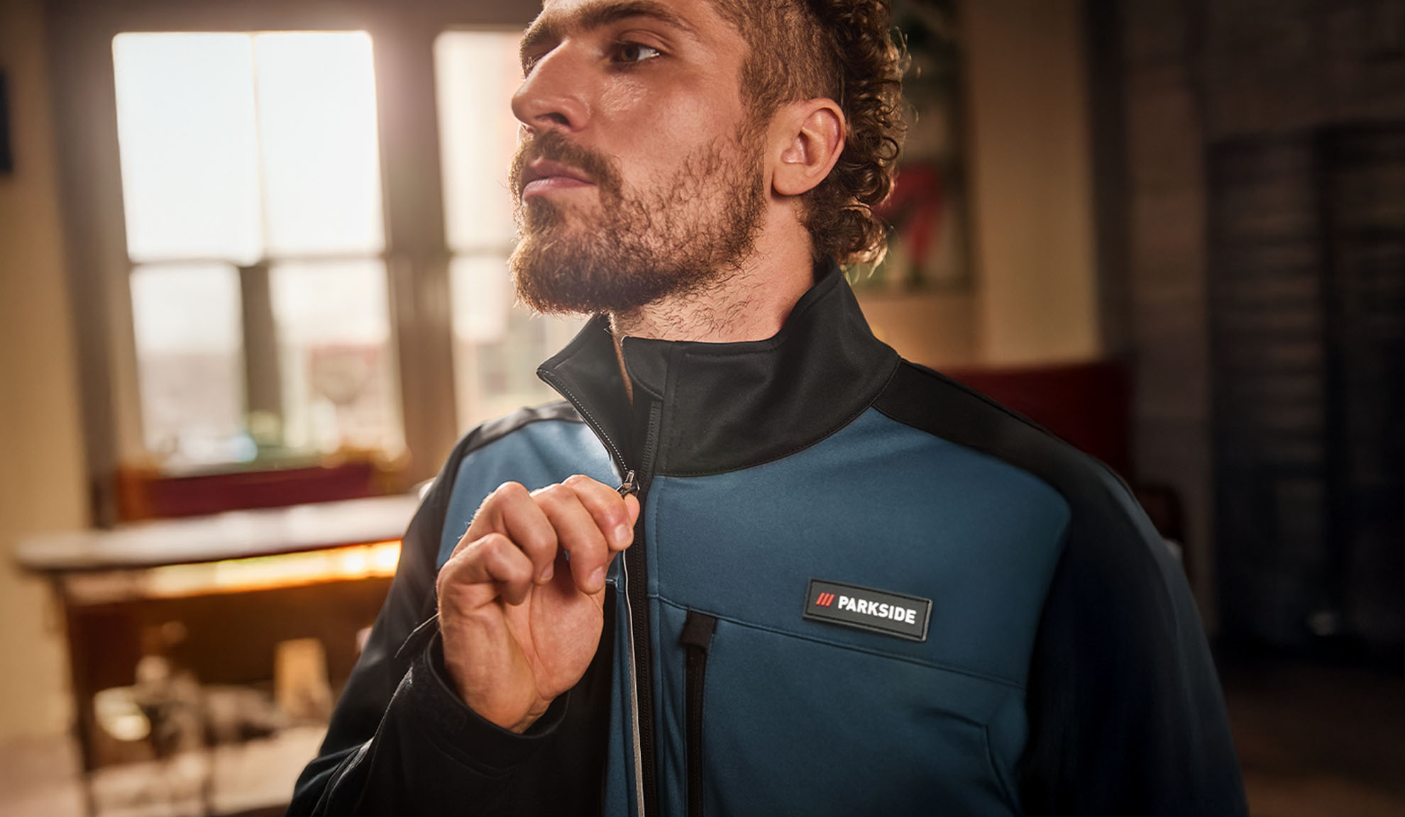 Vyras su mėlyna ir juoda Parkside darbo striuke, užsisegantis ją.
