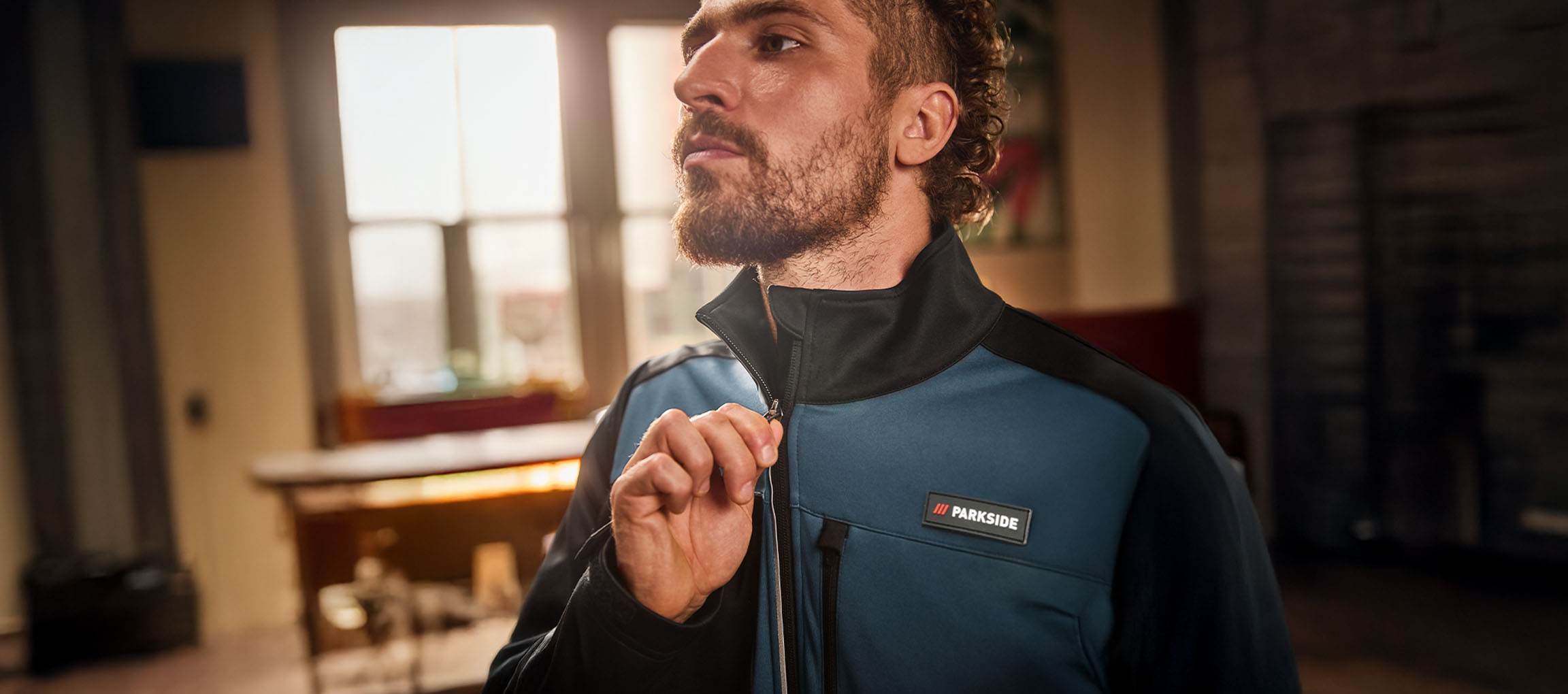 Vyras su mėlyna ir juoda Parkside darbo striuke užsisega ją