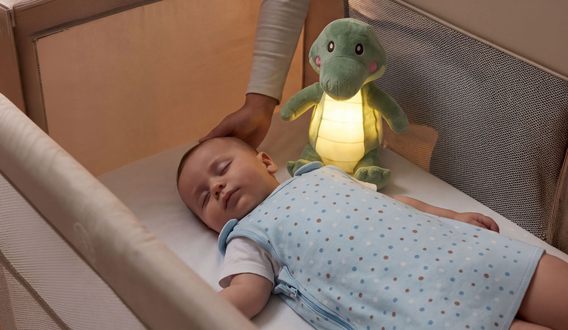 Kūdikis miega lovelėje su minkštu žaislu ir tėvų ranka.