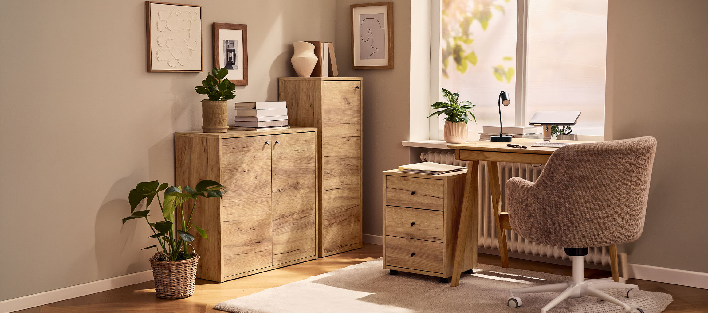 Namų biuras su medinėmis spintelėmis, stalu ir kėde, dekoruotas augalais ir paveikslais.