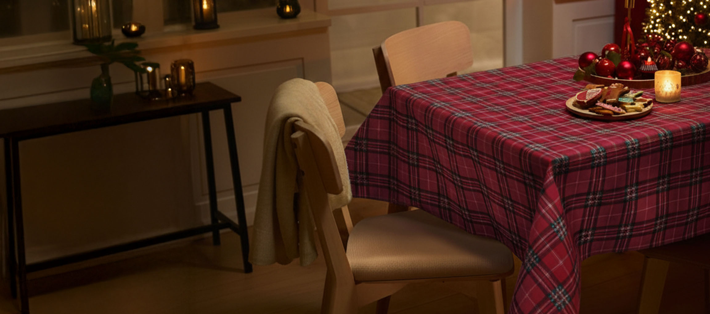 Kalėdinis stalo serviravimas su raudona languota staltiese, kėdėmis ir kalėdiniais sausainiais.