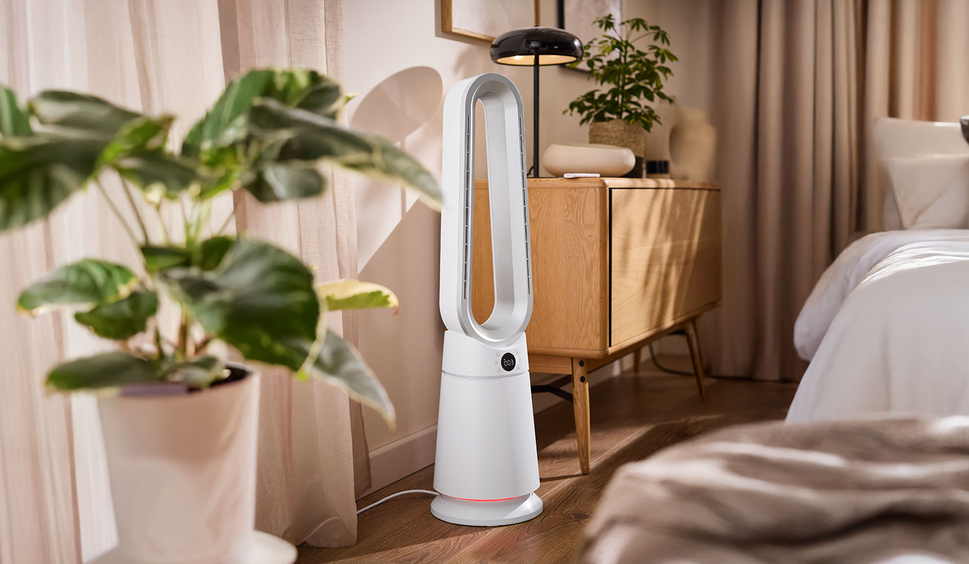 Baltas bokštinis ventiliatorius moderniame miegamajame su augalais ir mediniais baldais.