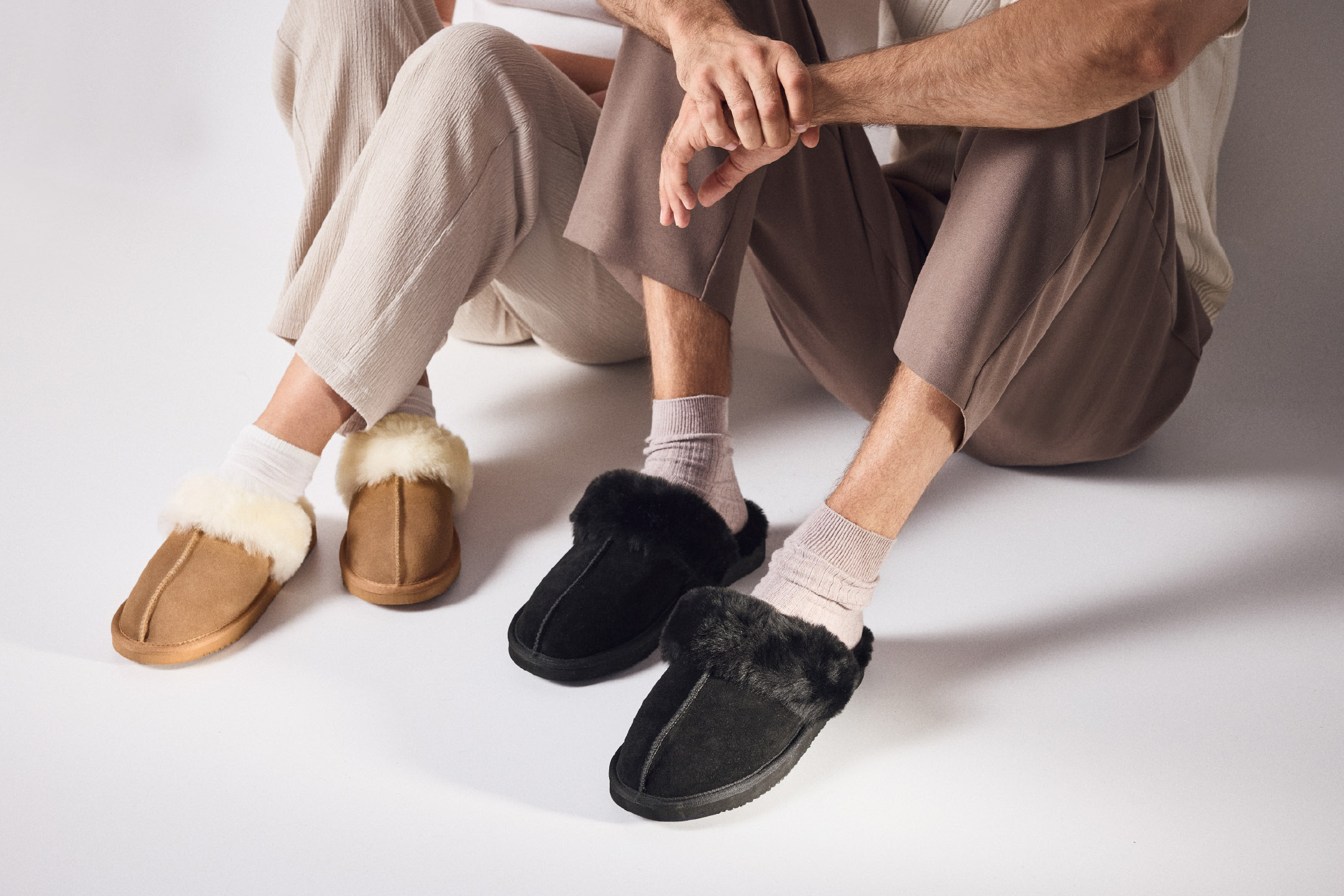 Dvi poros sėdi ant grindų, avėdami rudas ir juodas šlepetes.