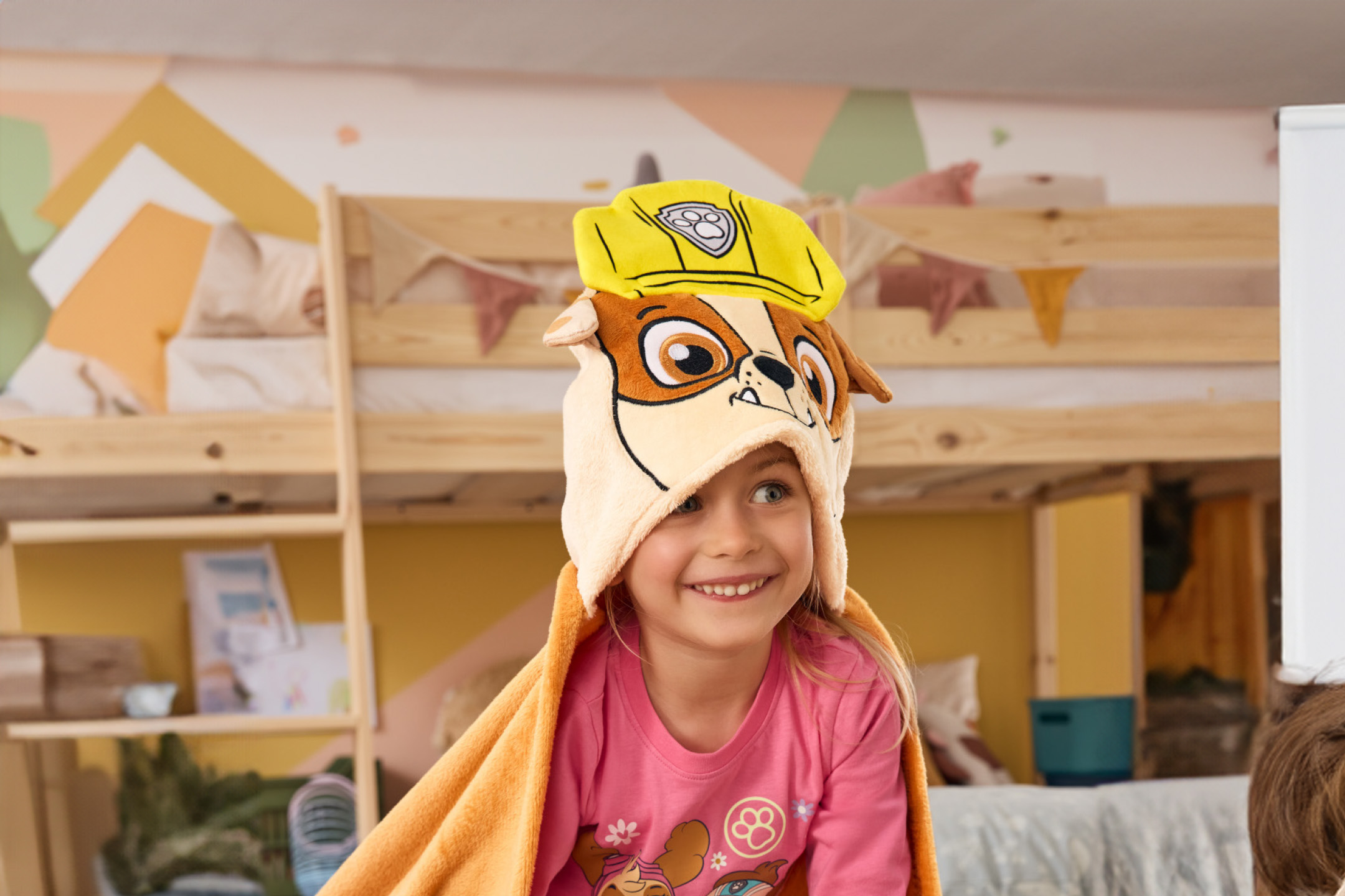 Mergaitė su „Paw Patrol“ Rubble rankšluosčiu ir pižama, šypsosi miegamajame.