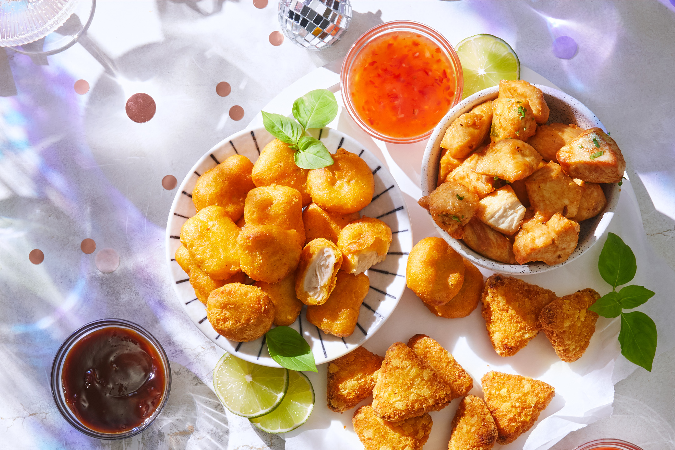 Vištienos gabalėliai, trikampiai bulvių kroketai ir padažai ant stalo su vakarėlio dekoracijomis.