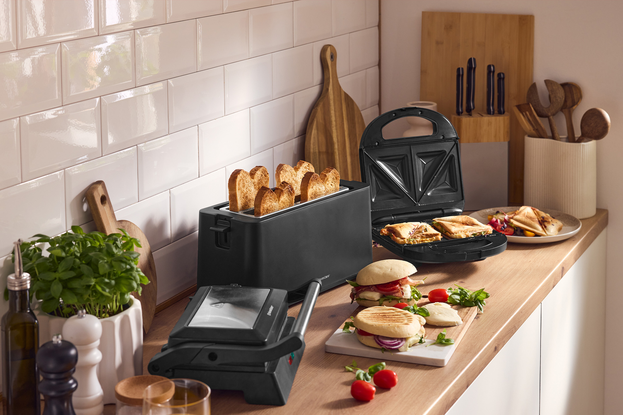 Virtuvės stalviršis su SilverCrest skrudintuvu, sumuštinių keptuve ir panini sumuštiniais.