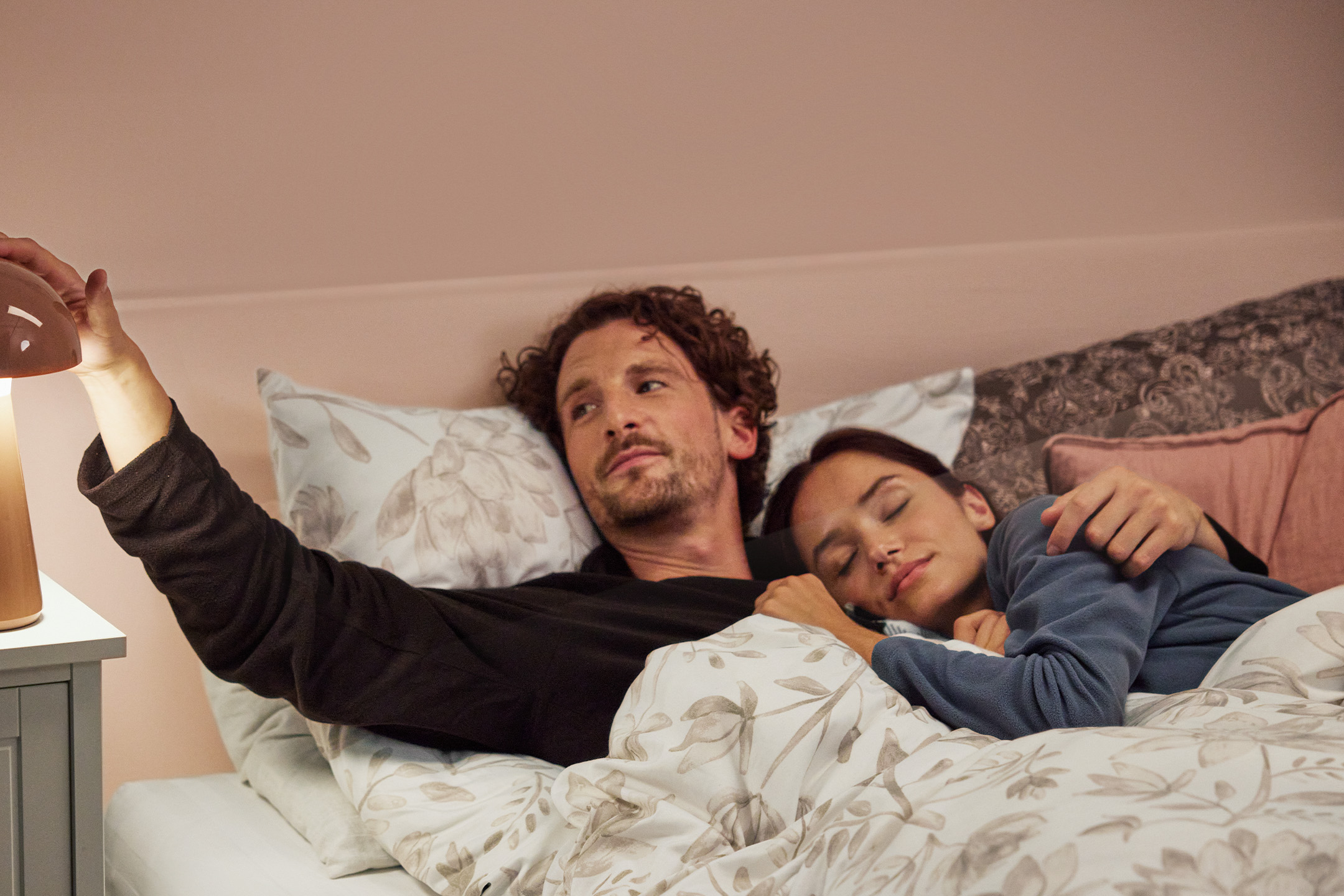 Pora lovoje su patalyne, vyras įjungia naktinę lempą.