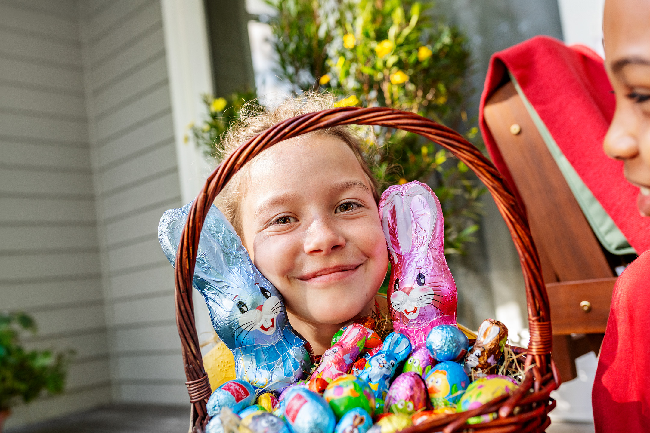 Šypsosi mergaitė su velykiniu krepšeliu, pilnu šokoladinių zuikučių ir kiaušinių.