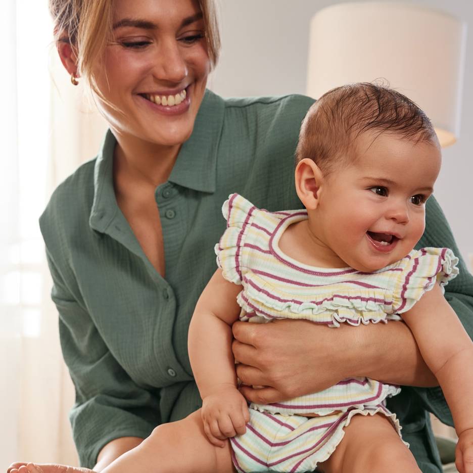 Besišypsanti mama su laimingu kūdikiu, dėvinčiu spalvingą dryžuotą aprangą.