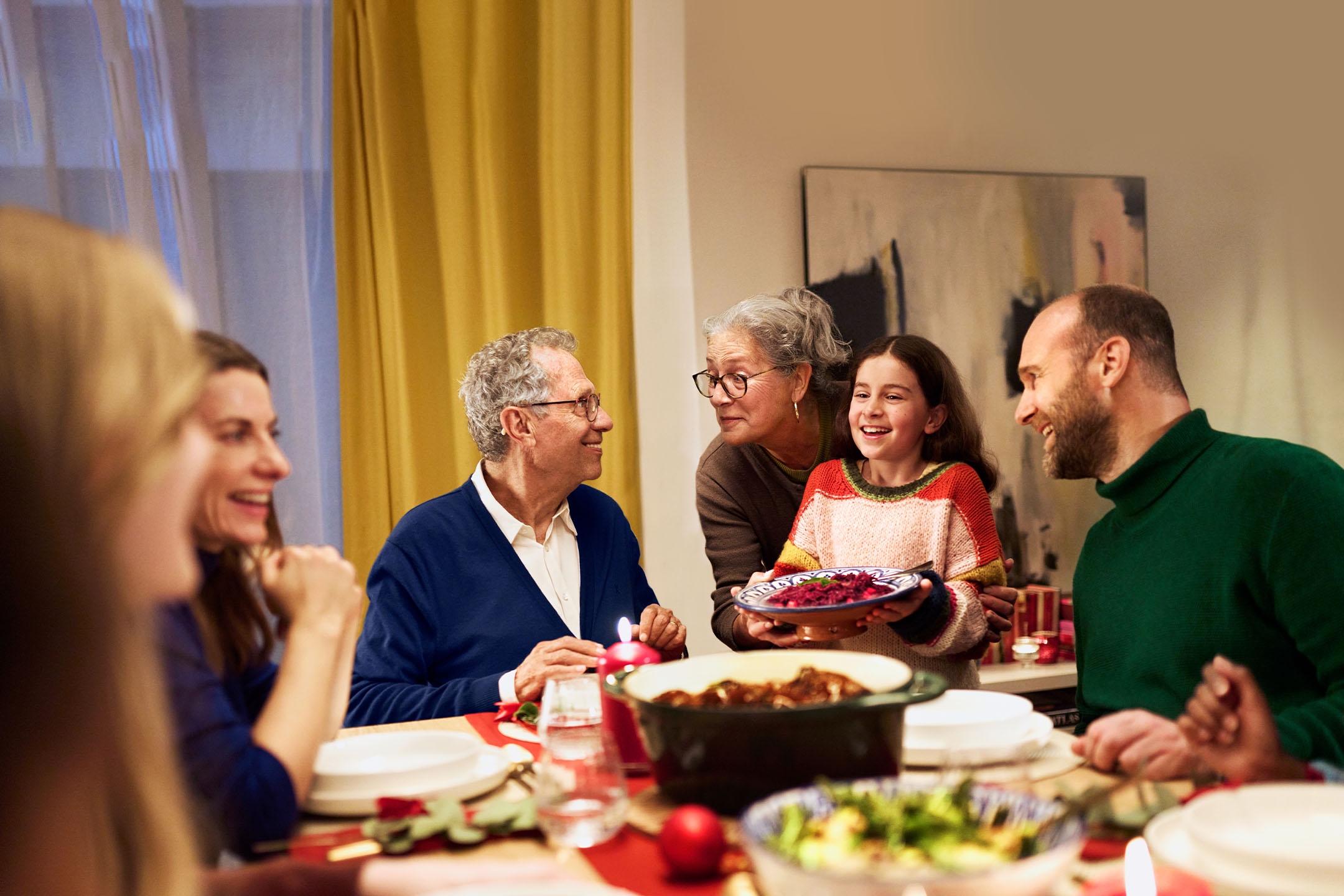 Šeima prie stalo, mergaitė laiko lėkštę su maistu, šventinė vakarienė.