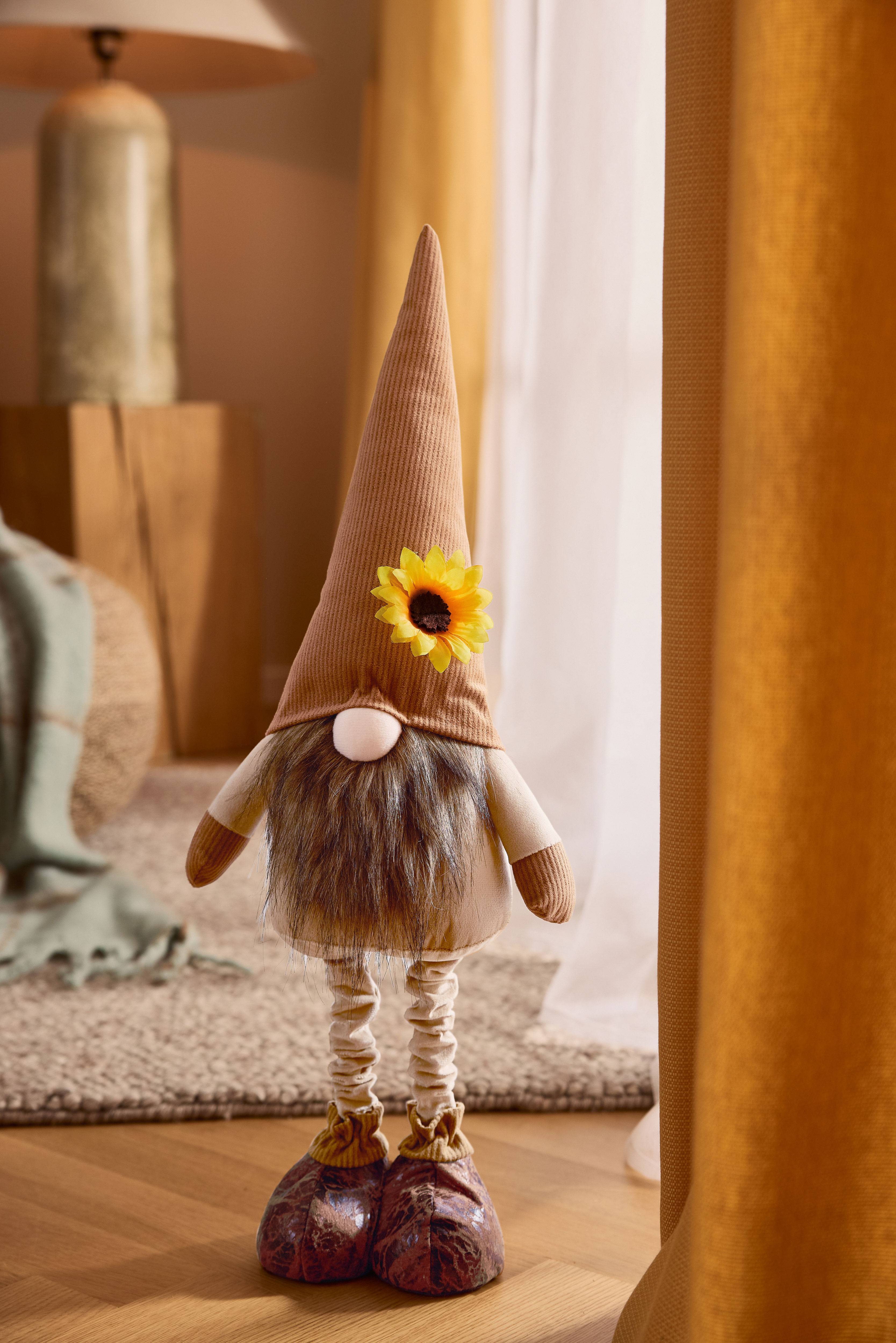 Pliušinis nykštukas su ruda smailia kepure, barzda ir saulėgrąža, jaukioje aplinkoje.