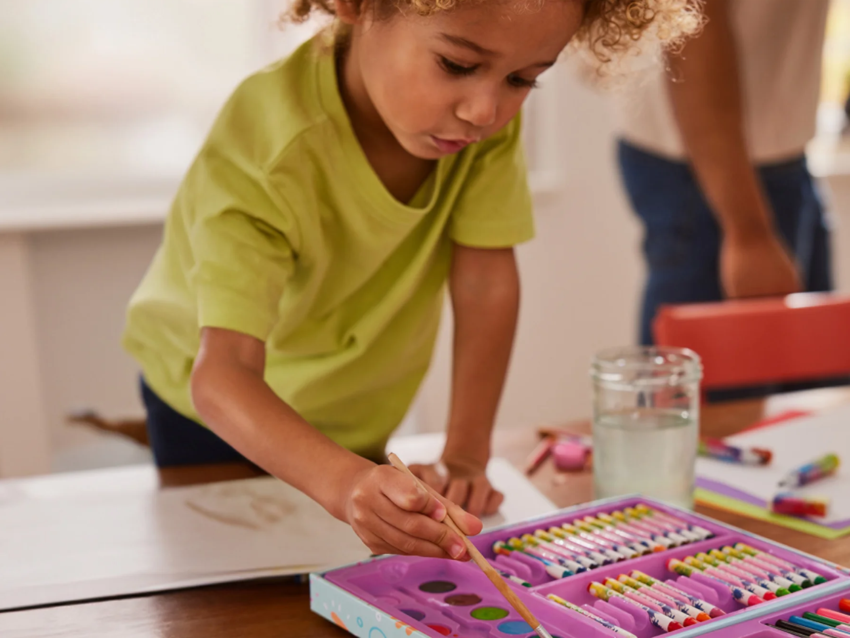 Vaikas piešia su spalvotais pieštukais ir dažais iš „Crayola“ rinkinio.
