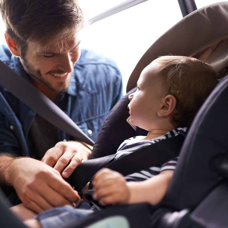 Tėvas tvirtina savo kūdikį automobilio kėdutėje.
