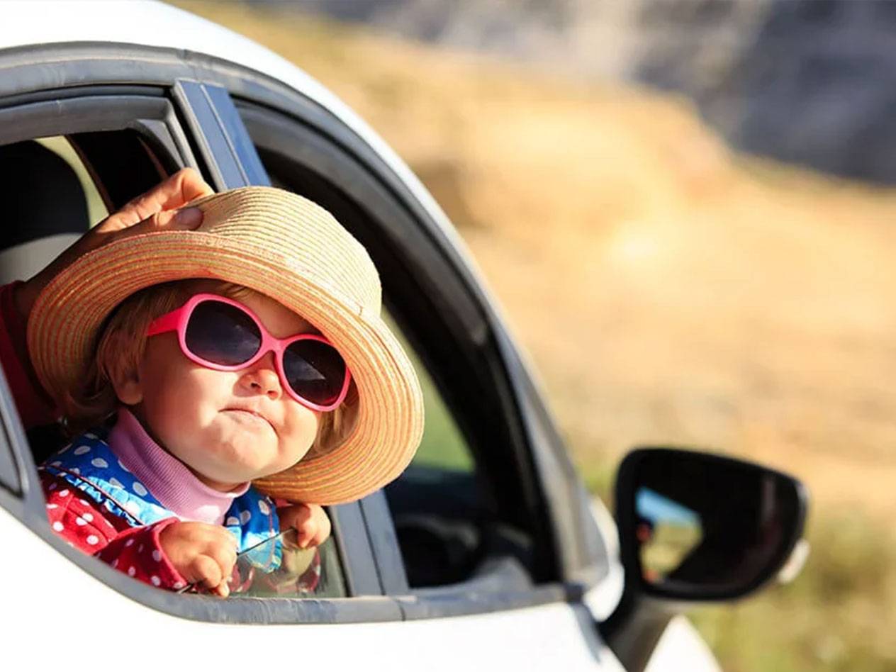 Mažas vaikas su kepure ir akiniais nuo saulės automobilyje.